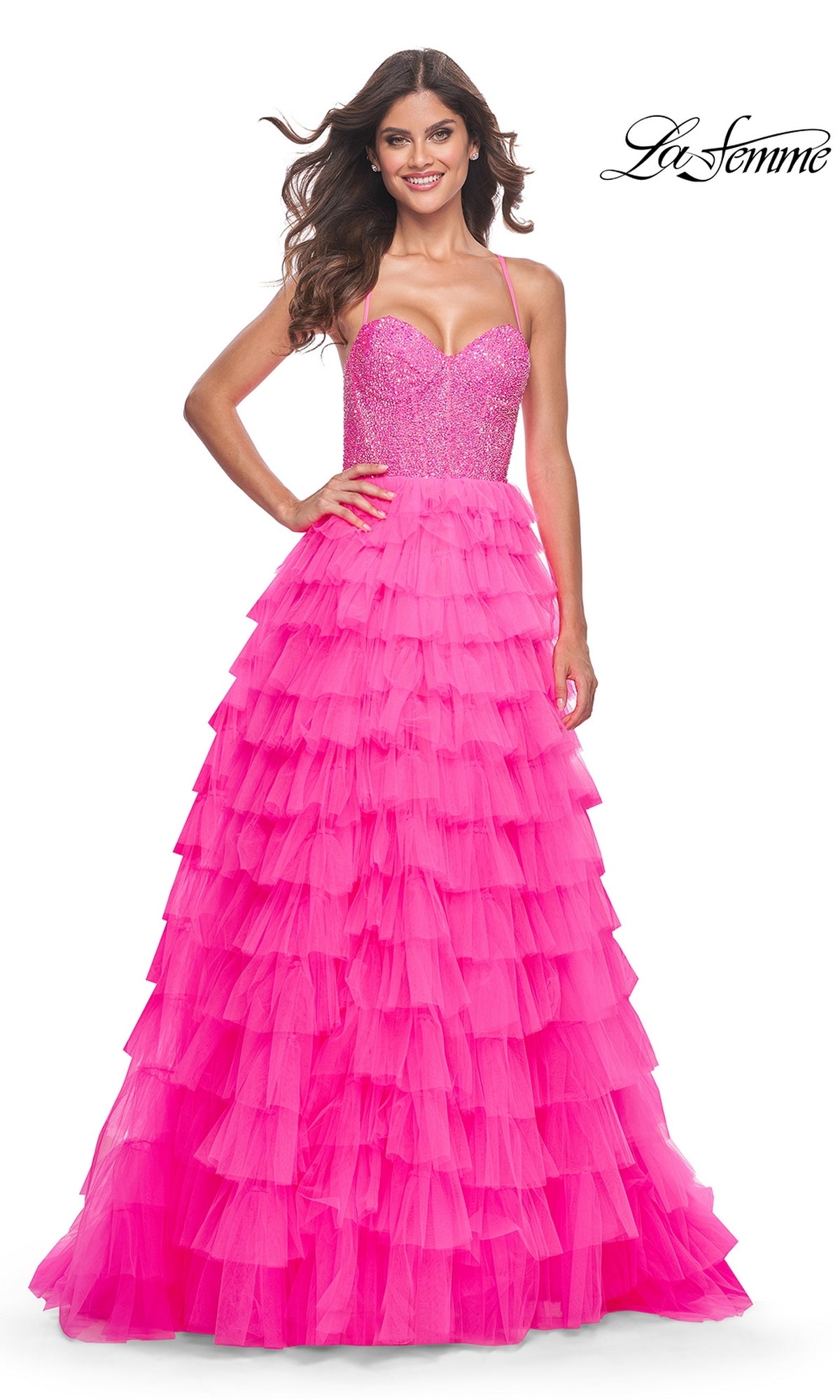 A woman smiles in the La Femme Long Tiered A-Line Prom Dress 32335, a bright pink, sleeveless, floor-length gown with a sparkling beaded sweetheart corset bodice and a tiered tulle skirt.
